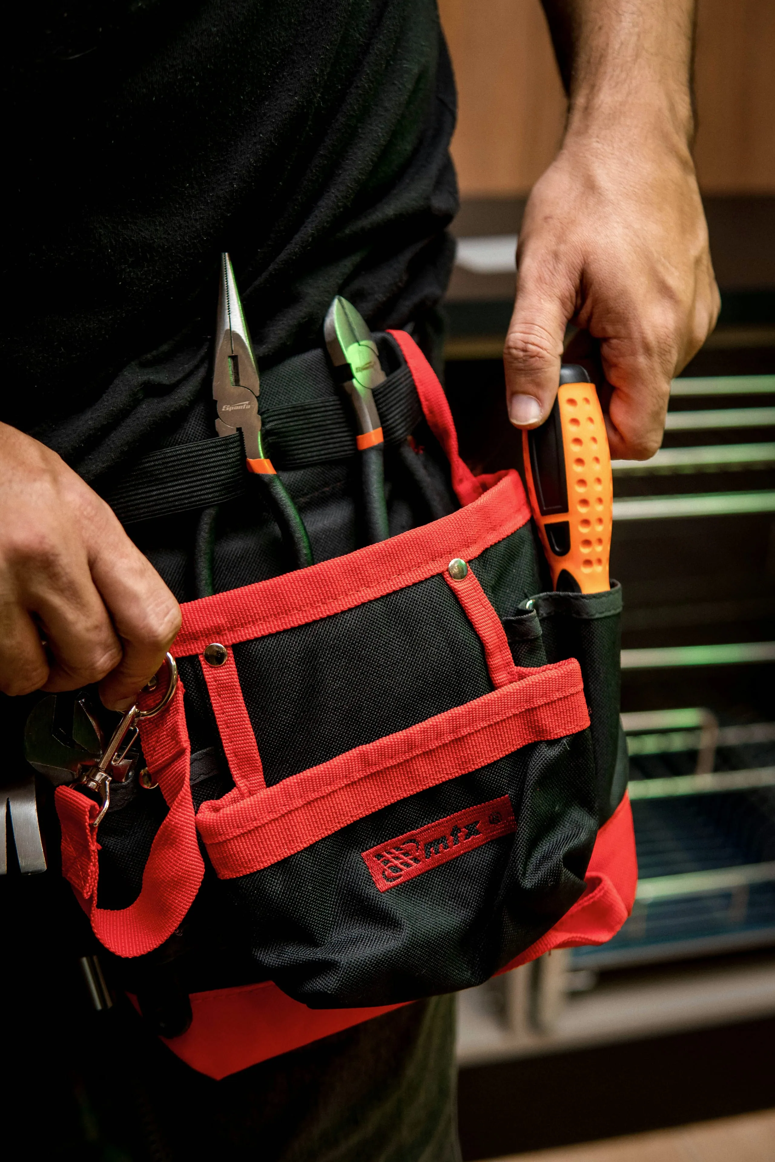 Hausmeister mit Werkzeugtasche am Gürtel, darin Zangen und ein Schraubendreher